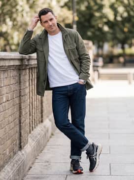 Gelventure 11 Extra Wide – Dark-wash straight-leg denim jeans rolled at the cuff, a crisp white organic cotton tee, and an olive green field jacket for a rugged casual weekend vibe.