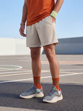 Giannis Freak 7 Ignition – Court Classic: Mesh basketball shorts in a neutral bone color, a deep orange graphic performance jersey to match the shoe's accents, and a lime green sweatband.