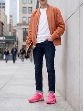 Dark denim jeans paired with a white t-shirt and an orange nylon bomber jacket to complement the shoe's accents.