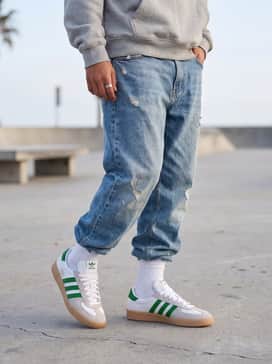 Glenburn Shoes – Baggy light-wash distressed jeans paired with an oversized graphic hoodie in a neutral grey and a matching green beanie.