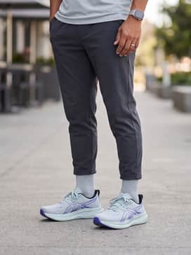 A clean athleisure look with slim-fit grey joggers, a crisp white oversized hoodie, and a black utility vest for a layered urban feel.