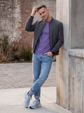 Glideride Max 2 – Streetwear-inspired pairing with tapered light-wash denim jeans cuffed at the ankle, a violet graphic t-shirt, and a charcoal bomber jacket.