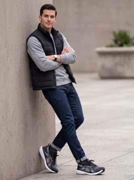 A weekend casual outfit pairing slim-fit dark indigo denim with a heather grey hoodie and a matte black puffer vest, emphasizing the shoe's sleek monochrome silhouette.