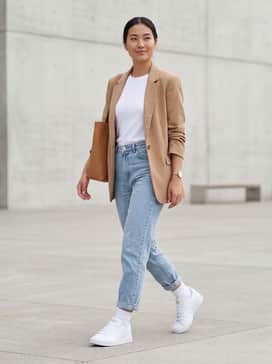 High-waisted light wash mom jeans, a tucked-in white organic cotton t-shirt, and a tan oversized blazer for a smart-casual office look.