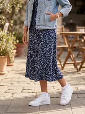 A navy blue floral midi dress with a denim jacket layered over the top and gold hoop earrings to match the shoe's branding.