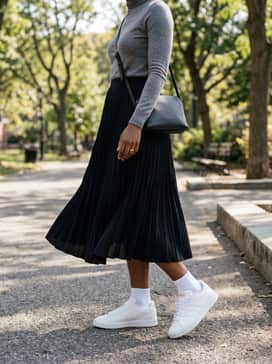 A black pleated midi skirt, a slim-fit grey turtleneck sweater, and a minimalist leather crossbody bag for a sophisticated outfit.