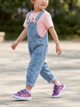Grand Court Adidas X Disney Minnie Mouse Kids – A soft pink graphic t-shirt featuring Minnie Mouse, paired with classic blue denim overalls and small white frilly socks for a timeless, adorable look.