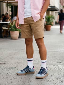 Grand Court Disney Shoes – Tan chino shorts paired with a pastel pink short-sleeve button-up shirt and high-cut white socks for a retro-preppy look.