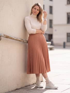 Gruuv – A midi-length pleated skirt in a soft terracotta hue topped with a cream-colored thin knit turtleneck sweater to balance the chunky sole with a feminine silhouette.