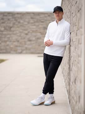 A sleek gym-to-street look with black tapered track pants, a white fitted quarter-zip pullover, and a matching gold-trimmed baseball cap.