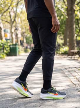 A gym-ready outfit consisting of matte black compression tights worn under loose athletic shorts, paired with a vibrant red sleeveless training tank.