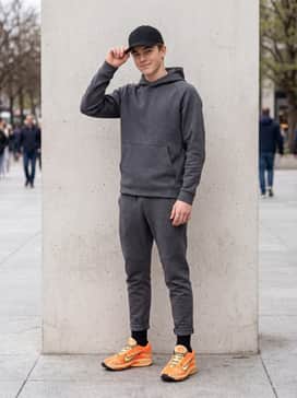 A sleek athleisure ensemble pairing charcoal grey tapered joggers with a matching tech-fleece hoodie and a black baseball cap for a balanced, modern silhouette.