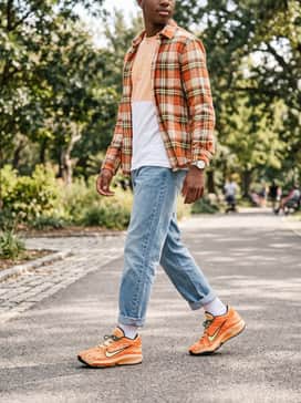 A bold casual weekend look consisting of cuffed light-wash distressed denim jeans, a plain white oversized t-shirt, and a flannel shirt with hints of orange worn open.