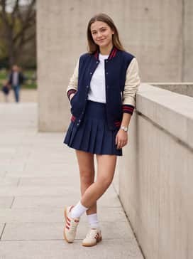 A navy blue pleated tennis skirt, white crew socks, and a matching cream-and-red varsity jacket for a preppy, sporty vibe.