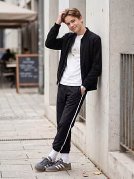 Black nylon track pants with a white side stripe, a vintage-style graphic tee, and a bomber jacket for an authentic 80s-inspired athletic aesthetic.