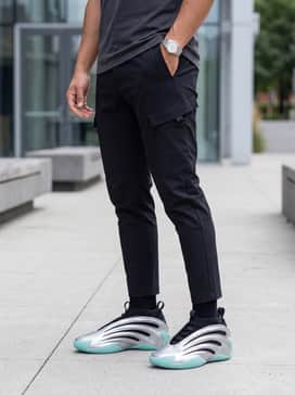 An urban techwear look consisting of tapered black tactical cargo pants with buckle details, a boxy charcoal grey heavyweight t-shirt, and a matte black utility vest.