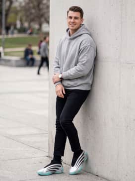 A casual streetwear outfit pairing stacked black slim-fit denim jeans with an oversized heather grey hoodie and a silver-toned minimalist watch to coordinate with the shoes.
