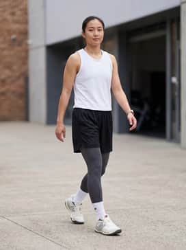 Black perforated mesh basketball shorts worn over charcoal compression leggings, paired with a white moisture-wicking team jersey and white crew-length athletic socks.