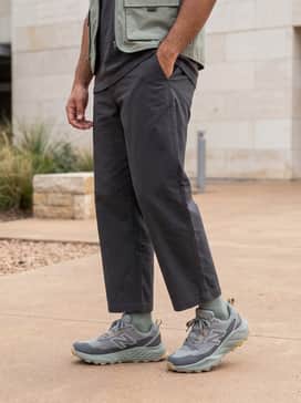 Wide-leg charcoal ripstop trousers with an oversized graphic tee and a beige utility vest to embrace a modern Gorpcore streetwear aesthetic.