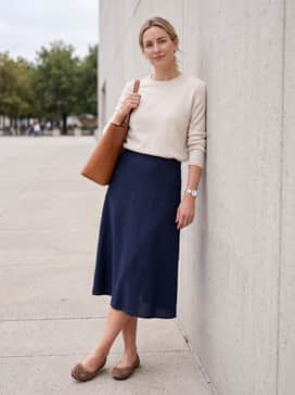 Classic navy blue tailored trousers and a cream lightweight cashmere sweater, finished with a structured leather tote bag for a polished business-casual ensemble.