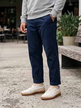 Navy blue tapered chinos, a grey melange crewneck sweatshirt, and a matching baseball cap to lean into a collegiate-inspired weekend vibe.