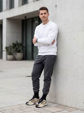 Tapered charcoal grey joggers worn with a white tech-fleece sweatshirt and high-performance black socks for a premium athleisure aesthetic.