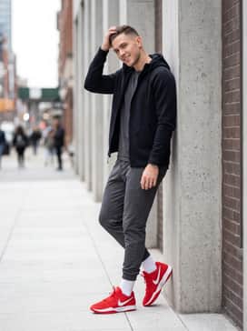 Ja 2 – A sleek athleisure ensemble consisting of charcoal grey tapered joggers and a fitted black tech-fleece zip-up hoodie, making the red sneakers the focal point.