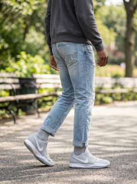 Ja 2 – Light wash distressed denim jeans worn with a simple heather grey crewneck sweatshirt and a charcoal baseball cap for an effortless, everyday casual ensemble.