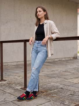 Light-wash distressed straight-leg jeans with a simple black tank top and a lightweight beige linen button-down shirt worn open for a relaxed vibe.