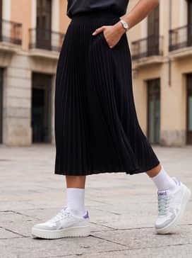 A black pleated midi skirt worn with a tucked-in oversized graphic t-shirt and white crew socks to emphasize the chunky platform silhouette.