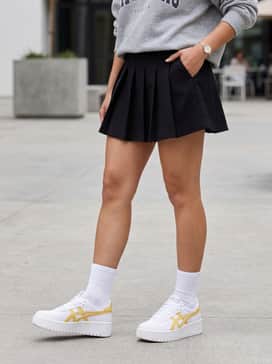 A black pleated tennis skirt with ruffled white crew socks and an oversized graphic sweatshirt for a trendy, athletic-inspired look.
