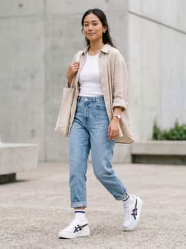 High-waisted mom jeans in a light wash, paired with a cropped white ribbed tank top and an oversized beige linen shirt worn open for a relaxed, summery look.