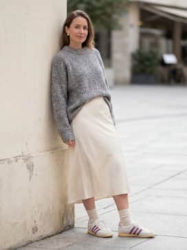 A cream-colored satin midi skirt worn with a chunky-knit oversized gray sweater for a mix of textures that highlights the sneaker's slim profile.