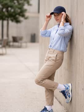Jog 100s – Tapered beige chinos combined with a tucked-in light blue button-down shirt and a navy baseball cap for a modern 'dad shoe' aesthetic.