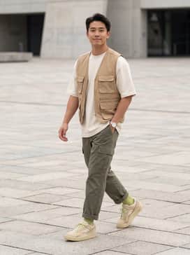 A pair of tapered olive green cargo pants paired with a heavyweight cream-colored oversized t-shirt and a matching tan canvas utility vest for a tactical street look.