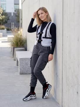 Futuristic Techwear: Tapered charcoal tech-fleece pants, a black moisture-wicking mock neck top, and a translucent white utility vest that mirrors the shoe's outer cage.