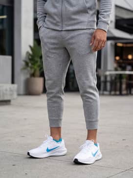 A modern athleisure ensemble consisting of heather grey tapered tech-fleece joggers, a matching slim-fit zip-up hoodie, and a cyan-blue baseball cap that picks up the color of the Nike swoosh.