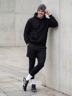 A cold-weather warm-up look consisting of thermal compression leggings under athletic shorts, topped with a heavy-duty team-branded hoodie and a beanie.