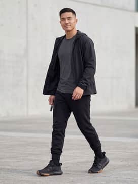 Black tapered tech-fleece joggers paired with a matching charcoal grey moisture-wicking performance tee and a lightweight windbreaker.