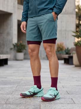An early morning running look consisting of dark burgundy thermal running tights, a heather grey long-sleeve base layer, and a lightweight, breathable water-resistant shell in a muted teal.