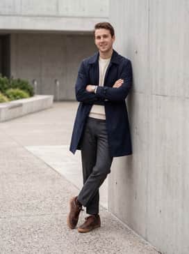 An effortless transitional ensemble with charcoal grey wool trousers, a cream-colored cashmere crewneck sweater, and a navy blue trench coat for a refined, layered aesthetic.
