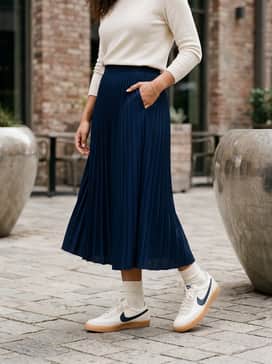 Killshot 2 – A navy blue pleated midi skirt styled with a tucked-in cream knit sweater and delicate gold jewelry for a polished daytime ensemble.
