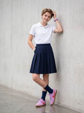 A preppy aesthetic pairing a navy blue pleated skirt or chino shorts with a tucked-in white polo and a lavender hair accessory or cap.