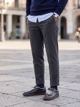 Tailored charcoal grey chinos worn with a light blue oxford button-down shirt and a navy blue merino wool sweater for a sophisticated casual office ensemble.