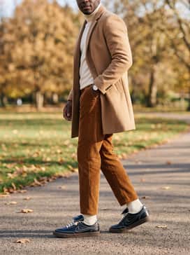 Tobacco-colored corduroy trousers paired with a cream-colored turtleneck and a tan wool overcoat for a rich, textured autumn outfit.