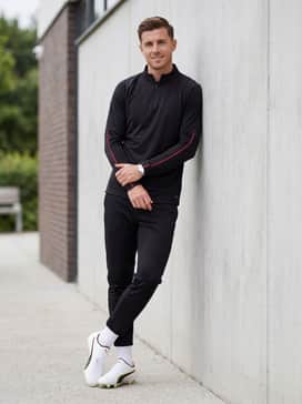 A sleek pre-game warm-up look comprising a black quarter-zip strike top with red sleeve details, tapered black track pants with ankle zips, and white crew-length performance socks.