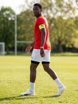 A bold club-style outfit using a vibrant red jersey to pick up the boot's subtle red trim, paired with white shorts and an electric lime captain's armband for a coordinated on-field aesthetic.