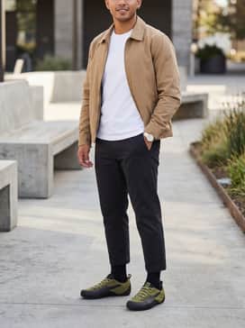 Klim Sneakers – Cropped charcoal grey chinos and a crisp white t-shirt layered under a tan harrington jacket for a clean, modern urban look.