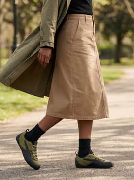 Klim Sneakers – A beige midi-length utility skirt with a black turtleneck and an olive green lightweight trench coat for a sophisticated, feminine techwear-inspired ensemble.