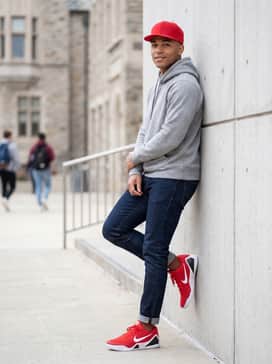 A casual weekend outfit pairing slim-fit dark indigo denim jeans with a neutral grey heavy-weight hoodie and a red snapback cap to tie the color scheme together.